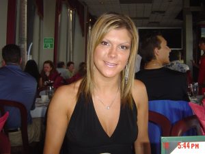 Woman in black halter top smiling in a crowded restaurant, diners and red chairs behind her.