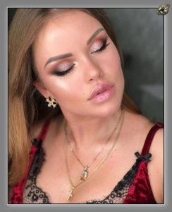 Close-up of a woman with eyes closed, bronze eyeshadow, gold necklaces and a red velvet top.