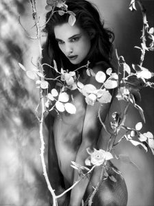 Black and white portrait of a dark-haired woman beside bare branches with small leaves.