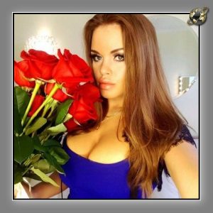 Woman with long brown hair in a blue top holding a bouquet of red roses indoors.