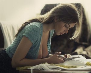 Woman in a teal knit top looking down at a notebook on a table beside a yellow measuring tape, soft warm light.
