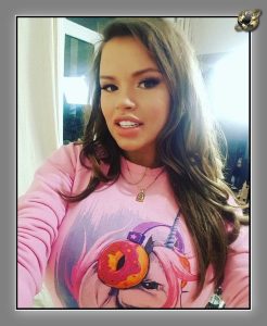 Woman with brown hair in pink sweatshirt with cartoon unicorn print, indoors.