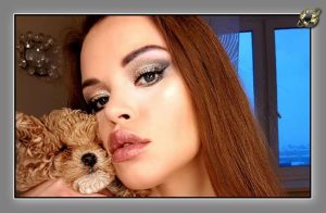 Close-up of a woman with shimmery eye makeup and a curly puppy resting against her cheek, blue window light behind.
