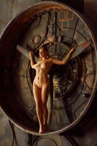 Nude woman standing within a large circular metal frame filled with pipes, gauges and brass mechanical parts, brown tones.
